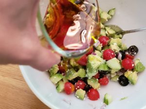 pouring oil and vinegar over other ingredients for Greek Cucumber Avocado Salad